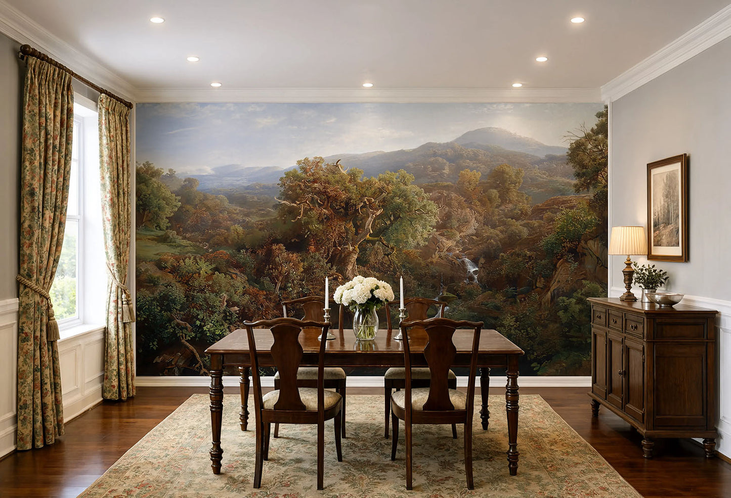 A large wall mural depicting a scenic mountain landscape with trees and hills, installed in a dining room behind a wooden dining table and chairs. The room has patterned curtains, a dark wood sideboard, and a beige rug.