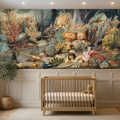 A large-scale underwater coral reef mural is displayed on a wall above a light wood crib in a styled nursery room with white wainscoting and a potted plant.