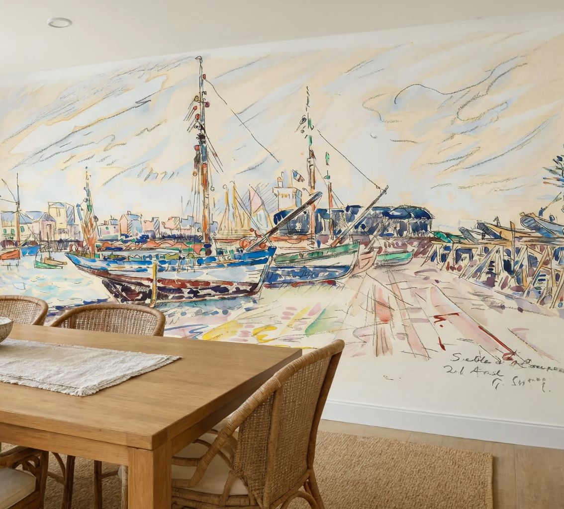 A large watercolor-style wall mural of a harbor scene with boats, docks, and buildings, shown in a dining room above a wooden table and chairs.