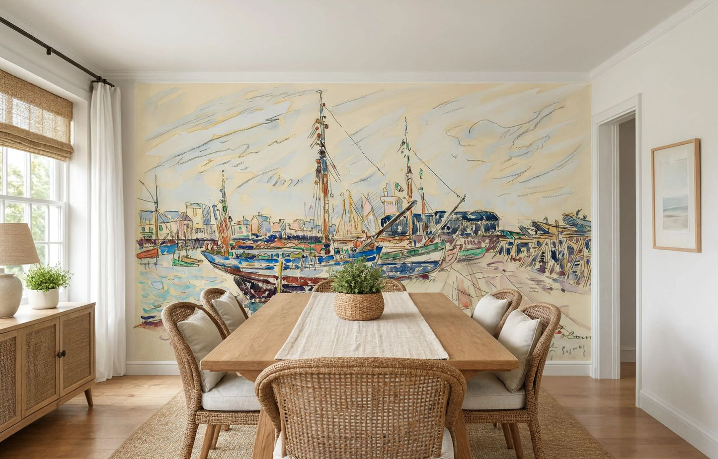 A large wall mural depicting a colorful harbor scene with sailboats and a pier, displayed on the back wall of a dining room with a wooden dining table and chairs.