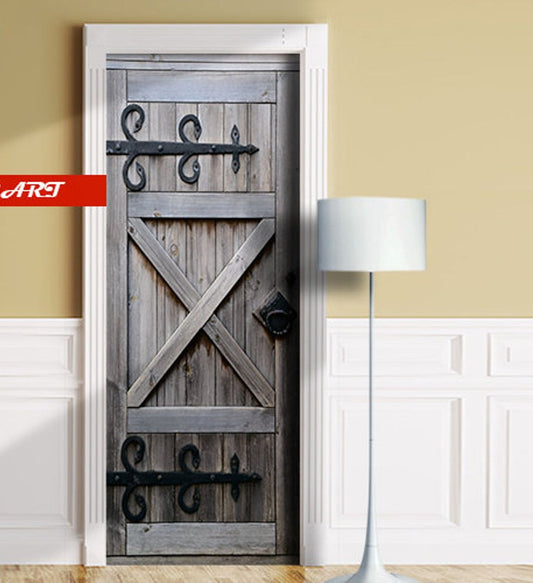 A rustic gray wooden barn-style door with black metal hinges and hardware, shown installed in a white door frame inside a room with beige walls and white wainscoting. A floor lamp stands to the right, and a red ART logo appears on the left.