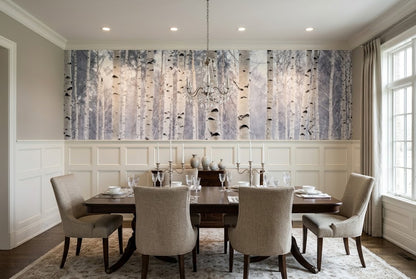 A large wall mural depicting a birch forest with white and gray trunks on a light background, installed in a dining room above a dark wood table and beige upholstered chairs.
