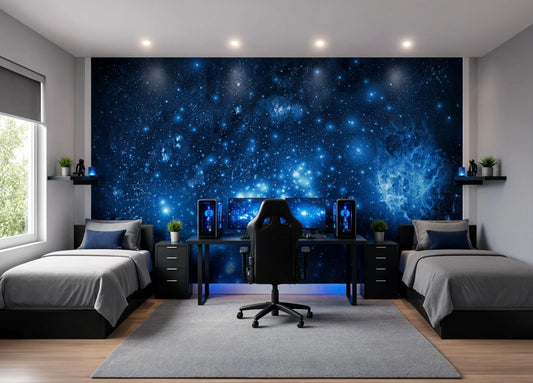 A modern gaming room setup featuring a large blue galaxy wall mural behind a desk with dual computer monitors and a black gaming chair, flanked by two single beds with gray bedding.