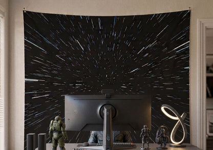 A large wall tapestry featuring a black  galactic starfield pattern, hanging in a home office setup behind a computer monitor with sci-fi action figures and a modern lamp.
