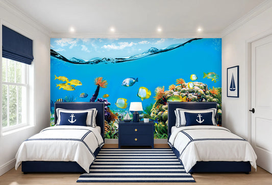 A styled children's bedroom featuring a large, vibrant underwater ocean wall mural with colorful fish and coral reefs behind two single beds with white and navy bedding.